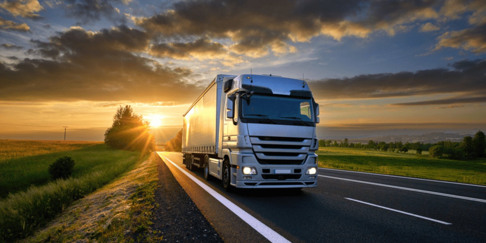 A European truck driving on a road with the sun setting in the background